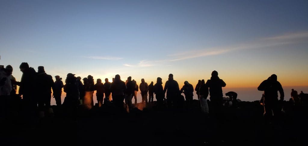 Trekkers standing at the summit of Mount Kilimanjaro at sunrise, witnessing breathtaking views from the top of Africa’s highest mountain in Tanzania.