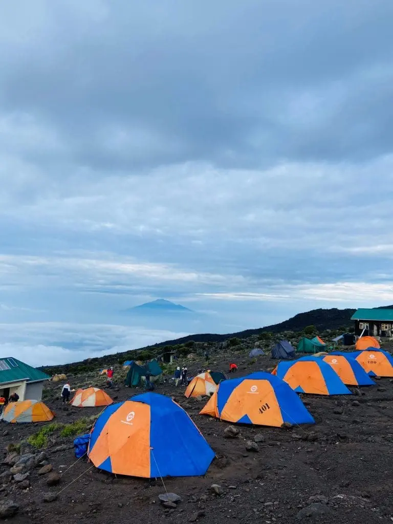 Zara Tanzania Adventures tents set up at Karanga Camp on Mount Kilimanjaro, overlooking clouds and distant peaks under a cool morning sky.
