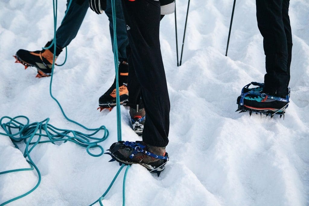 Climbers wearing crampons and using safety ropes while walking on a snowy mountain slope.