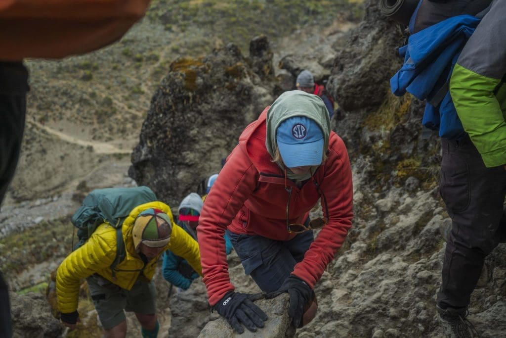 Trekkers climbing the rocky Barranco Wall on Kilimanjaro, carefully using their hands for support.
