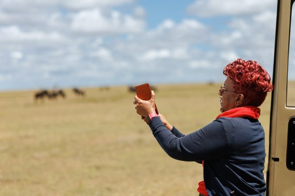 Zainab Ansell (Mama Zara) is taking a photo during a safari, smiling as she enjoys the wildlife view.