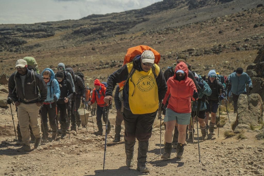 Zara Tanzania Adventures guides and climbers trekking up Mount Kilimanjaro, with porters carrying gear and supporting the team.