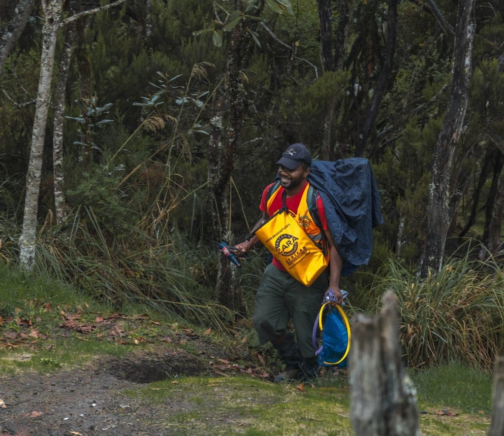 ara Tanzania Adventures porter weighing and collecting trash in a cleanup bag at a Kilimanjaro campsite as part of Leave No Trace practices.