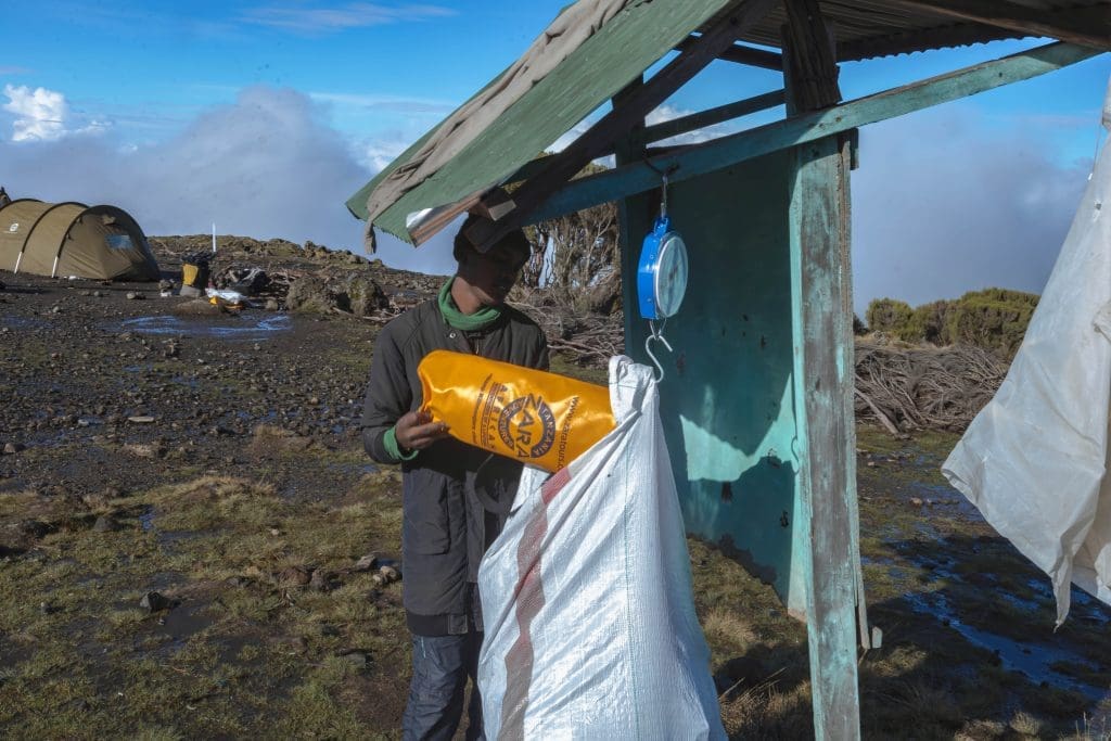 ara Tanzania Adventures porter weighing and collecting trash in a cleanup bag at a Kilimanjaro campsite as part of Leave No Trace practices.