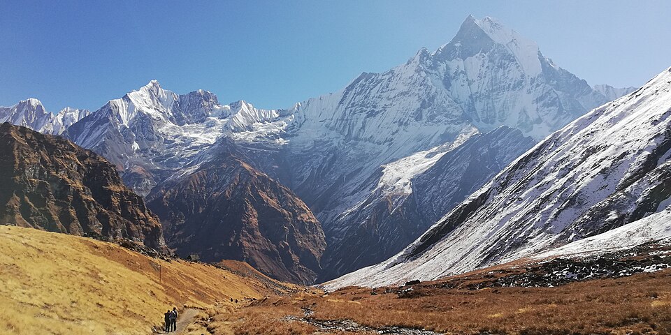 Aerial view of snow-covered mountains on the Annapurna Base Camp Trek under a clear blue sky.