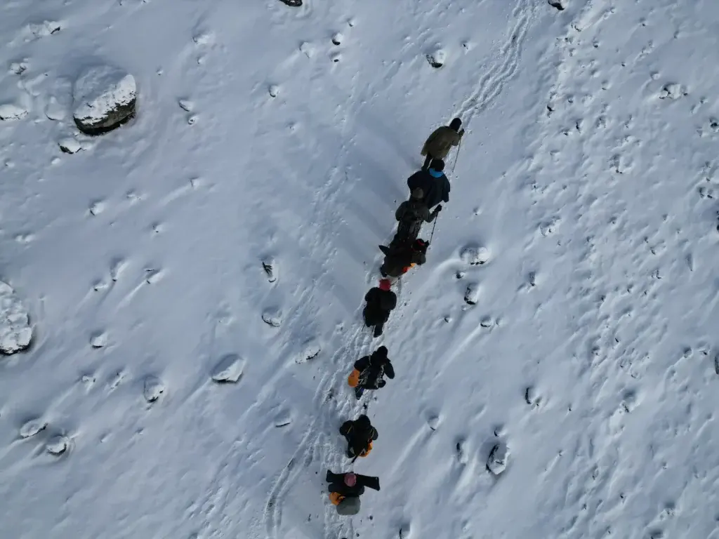 Aerial view of climbers trekking in a single line across the snow-covered slopes of Mount Kilimanjaro.