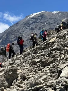 Trekkers ascending the rocky slopes of Mount Kilimanjaro with guides, showcasing the steep terrain and high-altitude landscape near the summit.