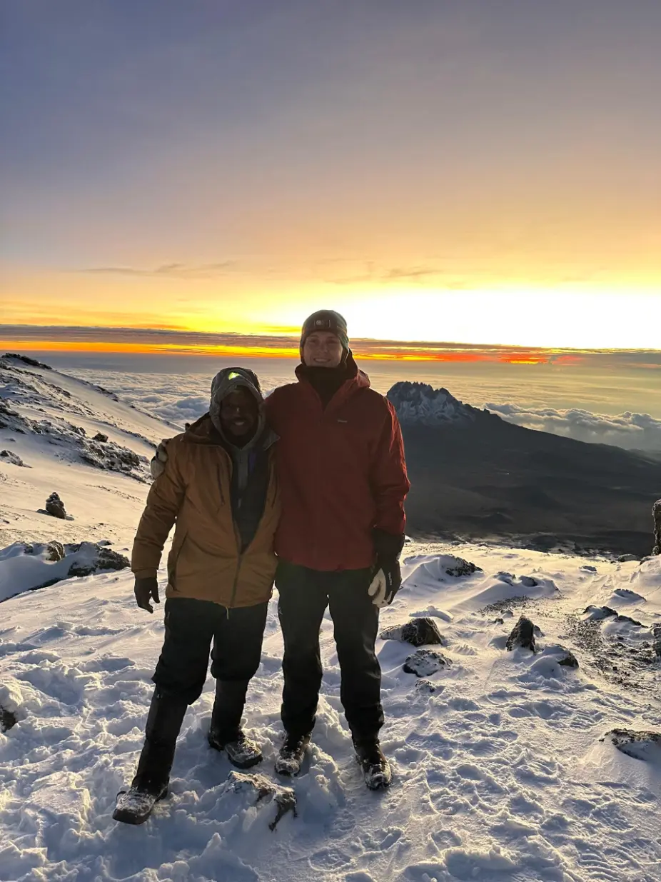 Zara Tanzania Adventures mountain guide with a climber at high altitude on Mount Kilimanjaro during sunrise, showcasing the snowy slopes near the summit at 5,895 meters above sea level.