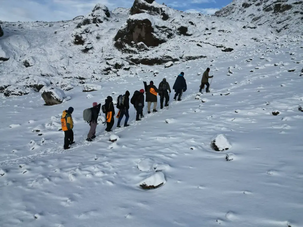 A group of trekkers hiking uphill on a snow-covered trail of Mount Kilimanjaro with rocky terrain in the background.