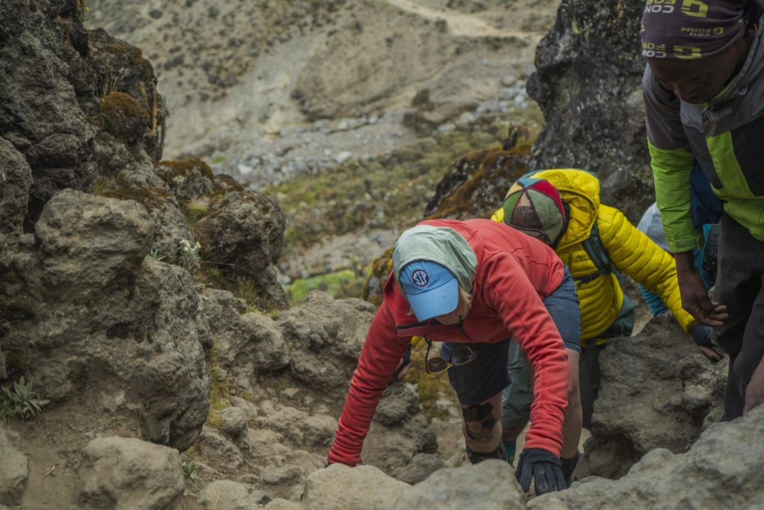 Climber scaling the Barranco Wall on Mount Kilimanjaro with assistance from a Zara Tanzania Adventures mountain guide.