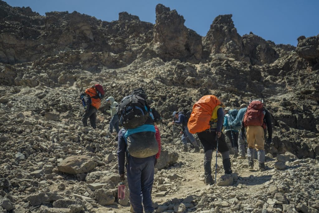 Climbers ascending a rocky trail on Mount Kilimanjaro carrying essential Kilimanjaro equipment and gear during a high-altitude trek.