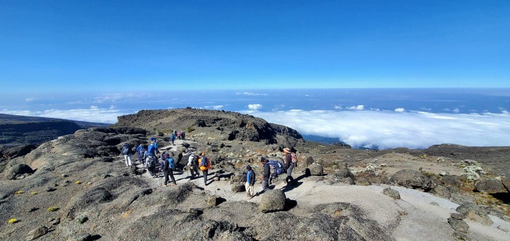 Hikers crossing Kilimanjaro’s rugged high-altitude ridge, drifting above the clouds like an old-world expedition with a modern adventure spirit.
