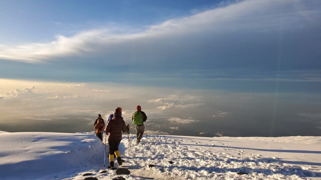 Trekkers walking across the snowy summit zone of Mount Kilimanjaro above the clouds, where extreme altitude and thin air increase the risk of altitude sickness.