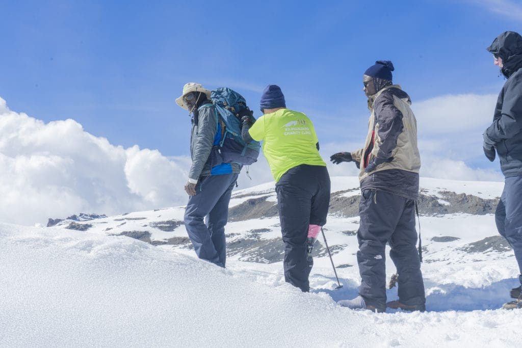 Climbers trekking through deep snow on Mount Kilimanjaro with guides assisting, high on the mountain near altitude zones above the glaciers.