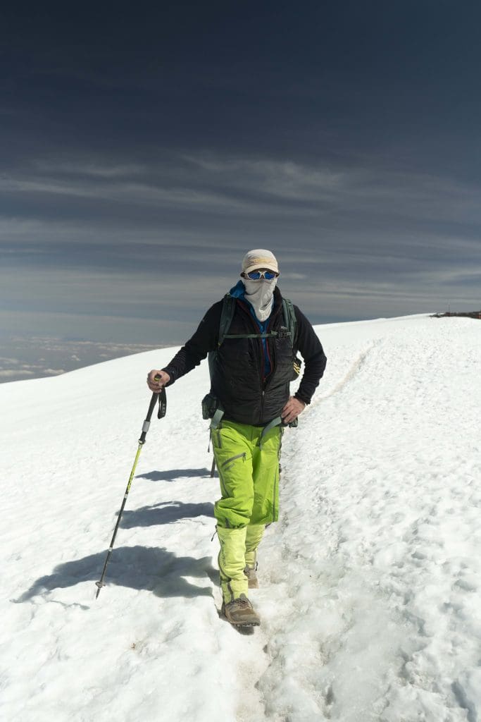 Climber trekking across snow near the summit of Mount Kilimanjaro using a walking pole at high altitude.